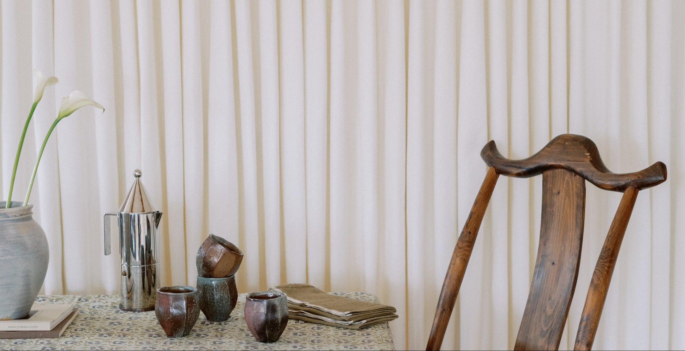 Wooden chair and table with decorative items against a white curtain background