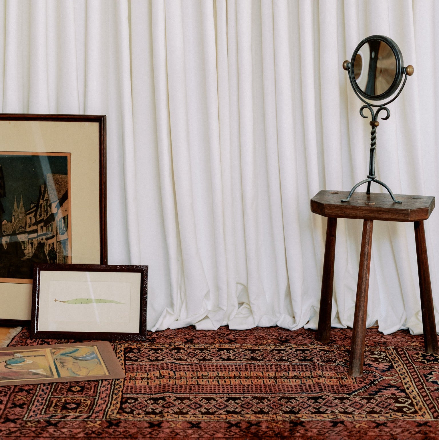 Framed artwork on a white wall with a wooden stool and mirror below.