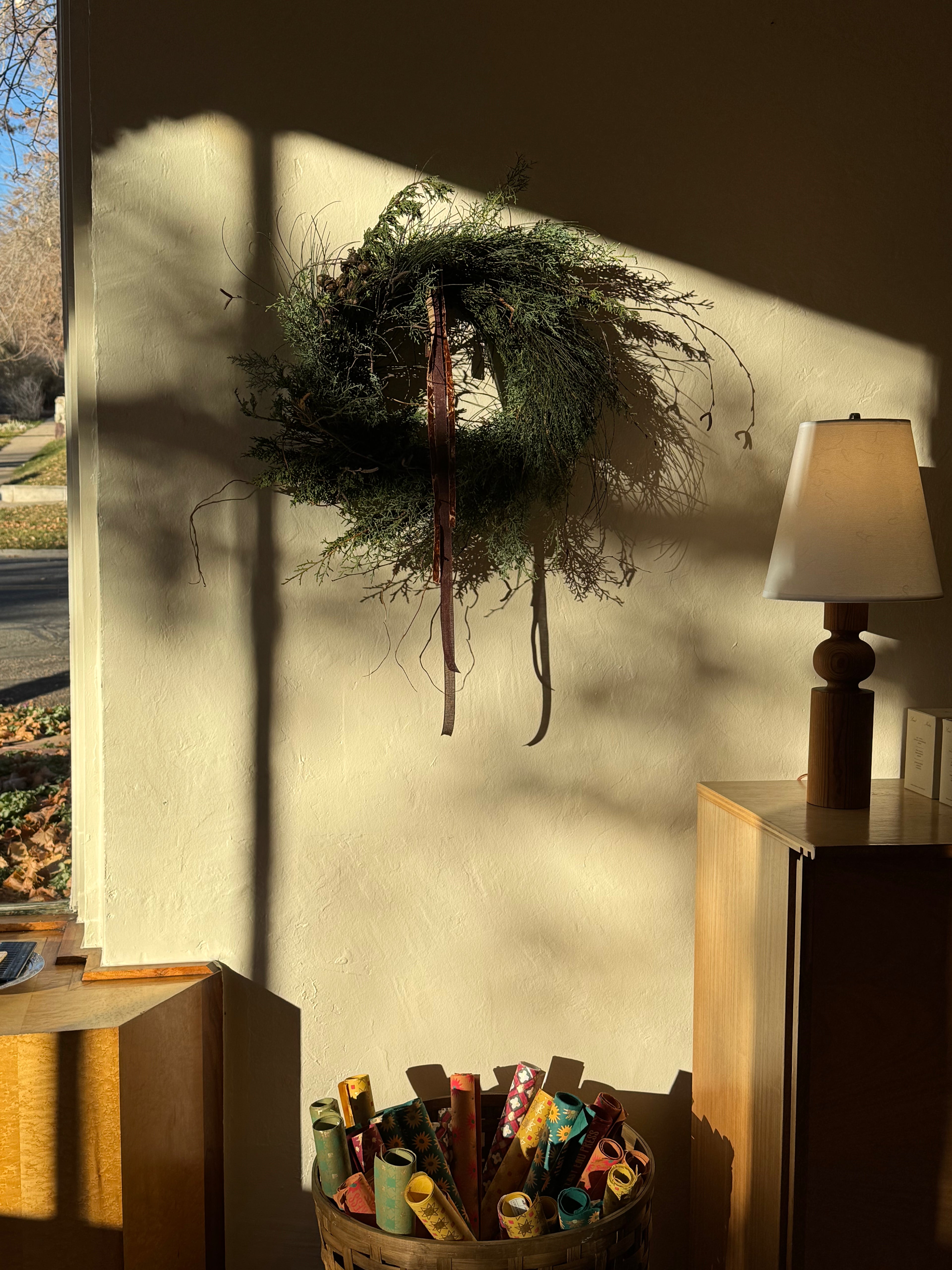 Wreath on a wall with a lamp and basket in the foreground